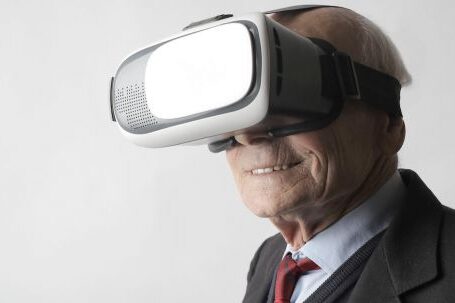 Ai-driven Innovations: Reality Unleashed - Smiling elderly gentleman wearing classy suit experiencing virtual reality while using modern headset on white background